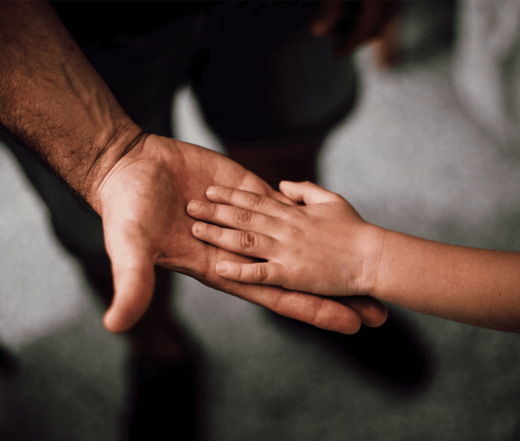 Close up photo of older man embracing a young child's hand, receiving a low-five.