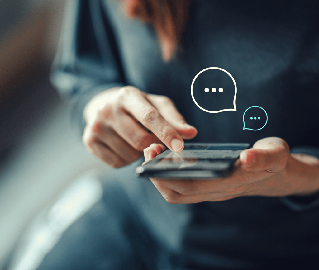 Close up photo of hands scrolling through a held mobile phone with chat bubbles popping out signifying that the person is talking via chat with someone.