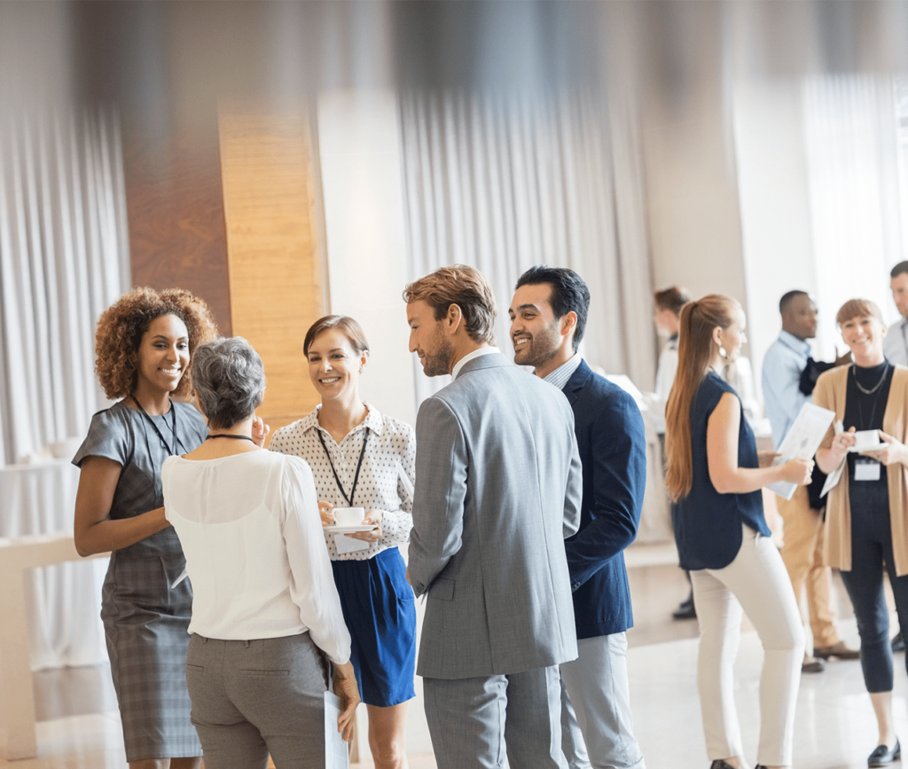 Multiple business professionals wearing their lanyards and mingling at a professional conference.