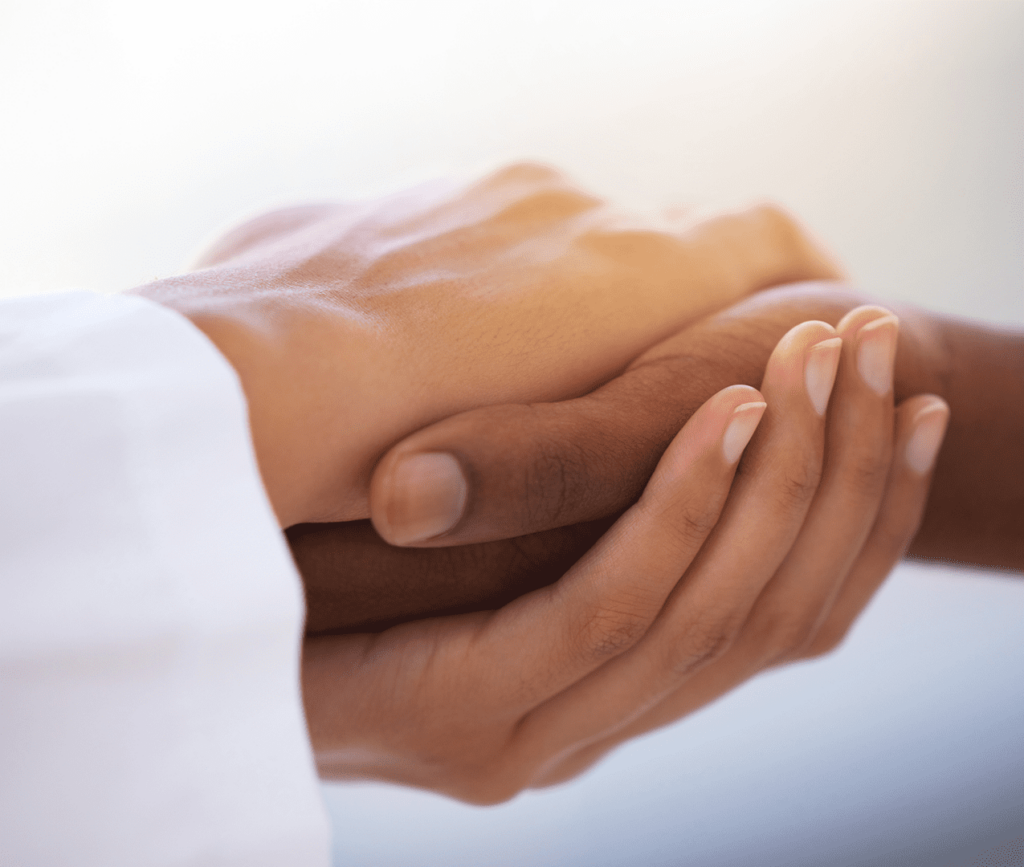 Close up of doctors hand holding a patient's hand compassionately as they navigate the challenges of medicine.