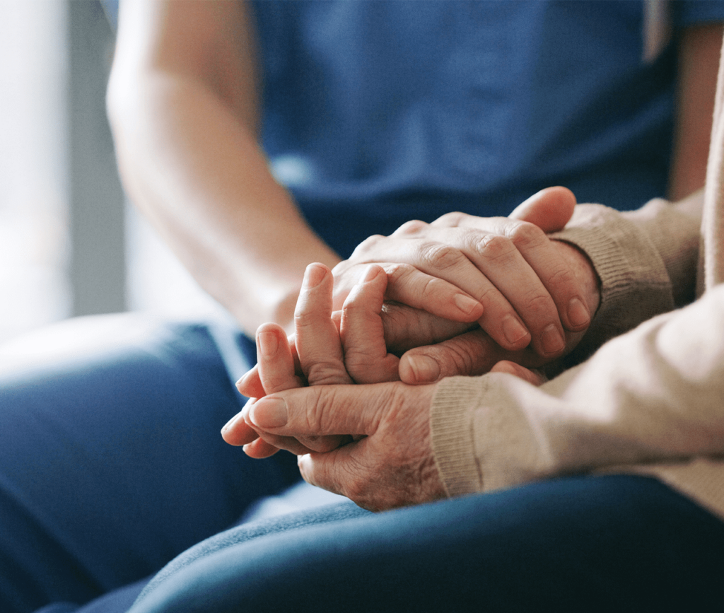 Close up of a doctor's hands compassionately placed over a patient's hands during a tough appointment.