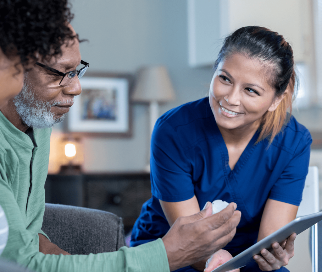 Friendly, at-home nurse presenting a tablet to her elderly patient who looks at a prescription bottle