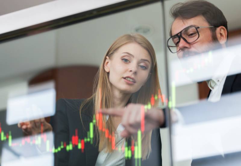 Businesswoman and businessman point to a waterfall chart displaying green and red data points on a computer.