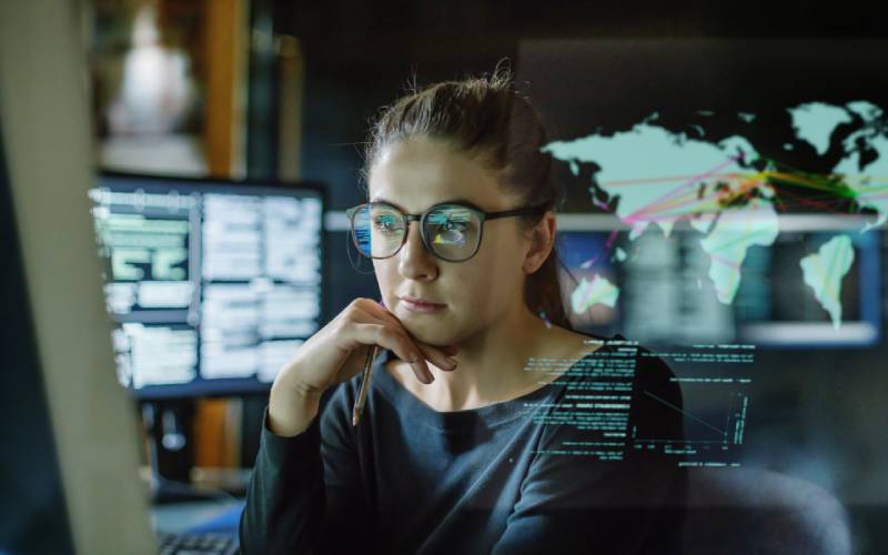 Young woman sits at her desk, surrounded by monitors and analyzes the data on each