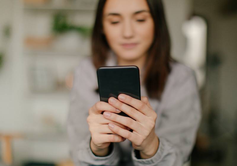 Close up of a young woman holding her cellphone and typing from her chair.