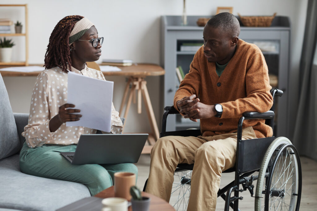 Patient in wheelchair having a consultation with a woman on her computer and holding documents.