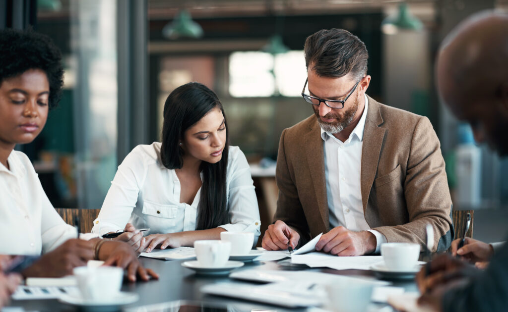 Middle-aged man reviews a document with his client at a table while two other colleagues take notes.